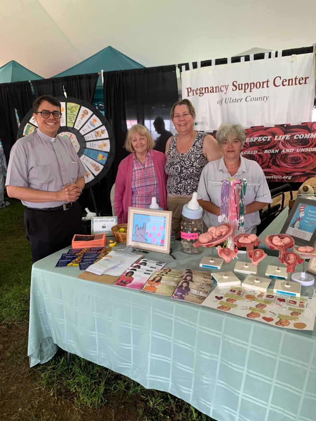 Fr. Arthur Rojas, Jane Randazzo (2nd from Left) and Catherine Parrinello (At far right) join Michelle Whittaker (2nd from right) at the joint booth of the Bravo Center and U.D.R.L.C.  Credit to U.D.R.L.C. for picture.